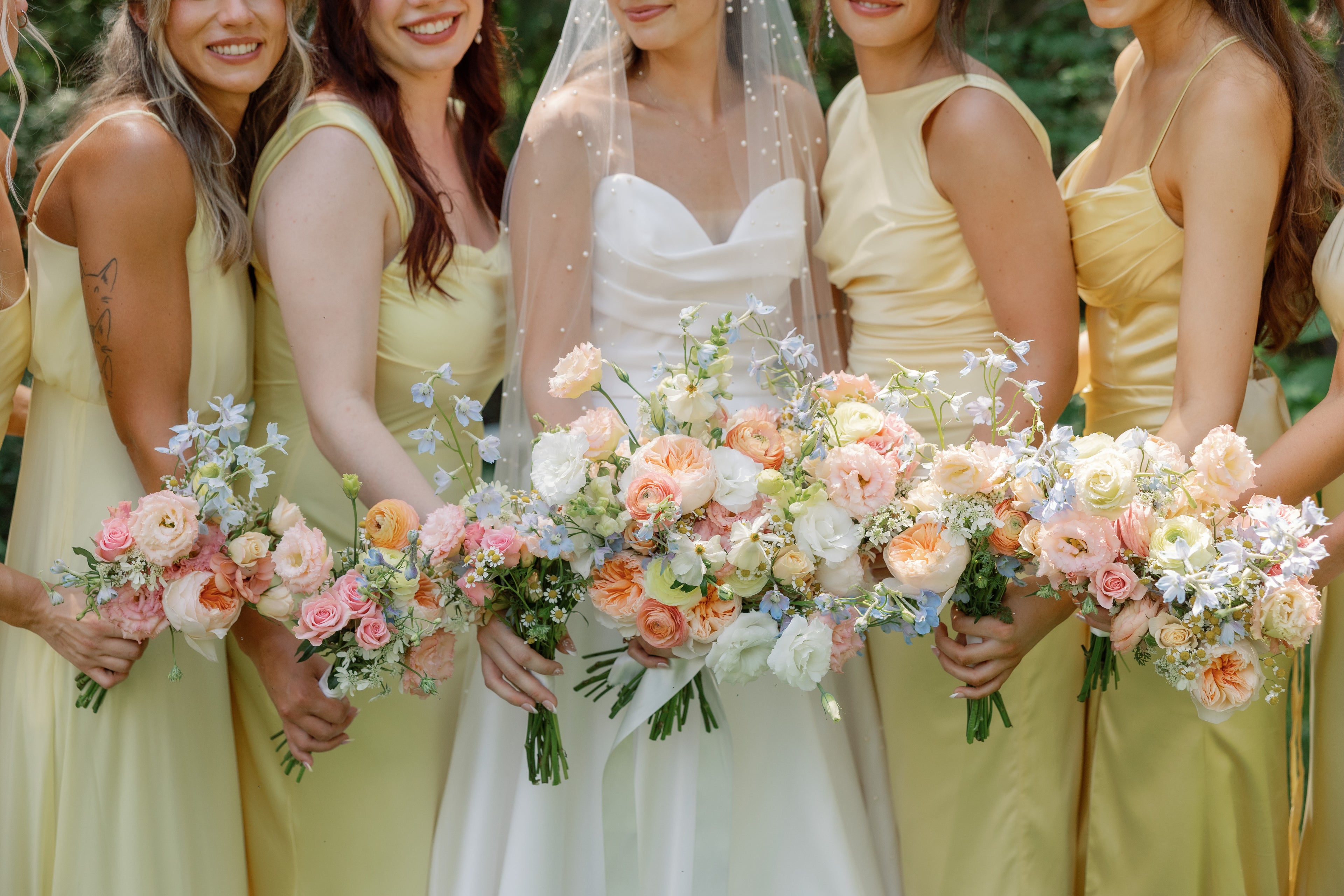 Bride with bridesmaids in yellow dresses holding floral bouquets.
