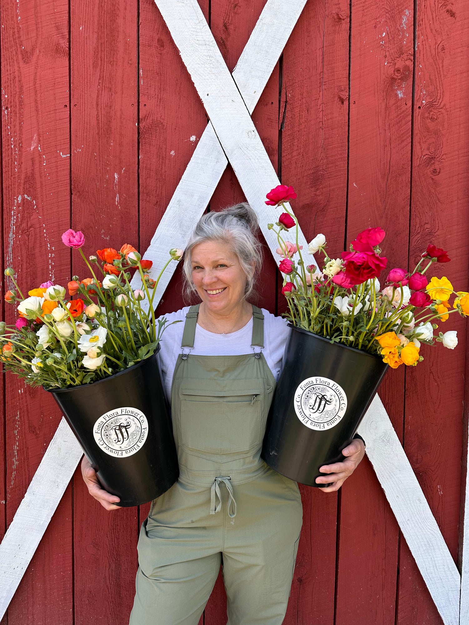 Person holding two large flower buckets in front of a red barn door