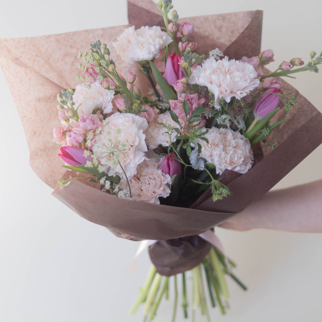 A lush and vibrant bouquet featuring an assortment of pinks and greenery, wrapped in natural paper and tied with a ribbon for a thoughtful Valentine’s Day.