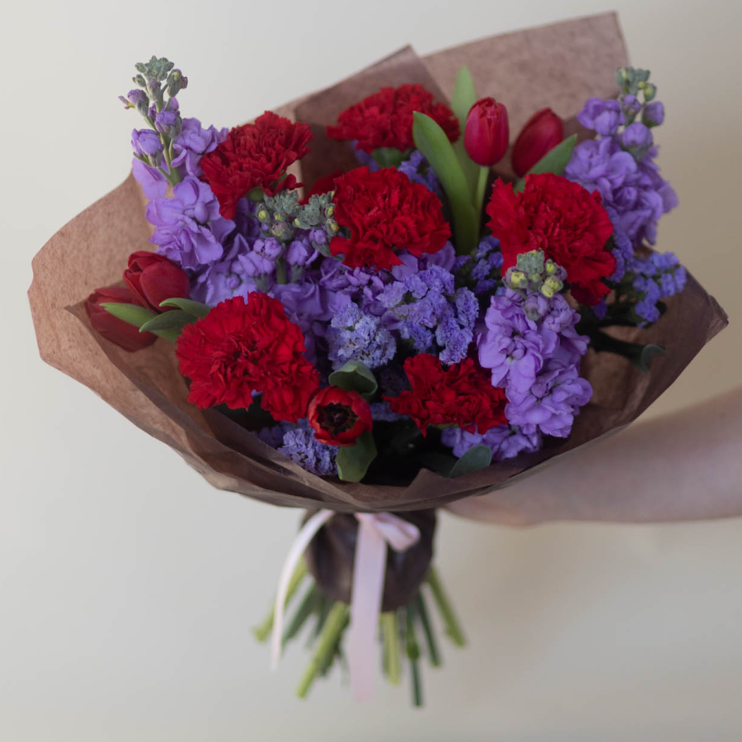 A romantic bouquet of deep red s and purples wrapped in elegant paper and finished with a ribbon for Valentine’s Day.